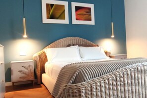 Ein Schlafzimmer mit einem Rattan-Kopfstück, weißer Bettwäsche und zwei Wandleuchten.