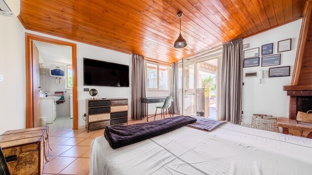 Un dormitorio con cama, techo de madera, televisor, escritorio, silla y vista a través de un ventanal.