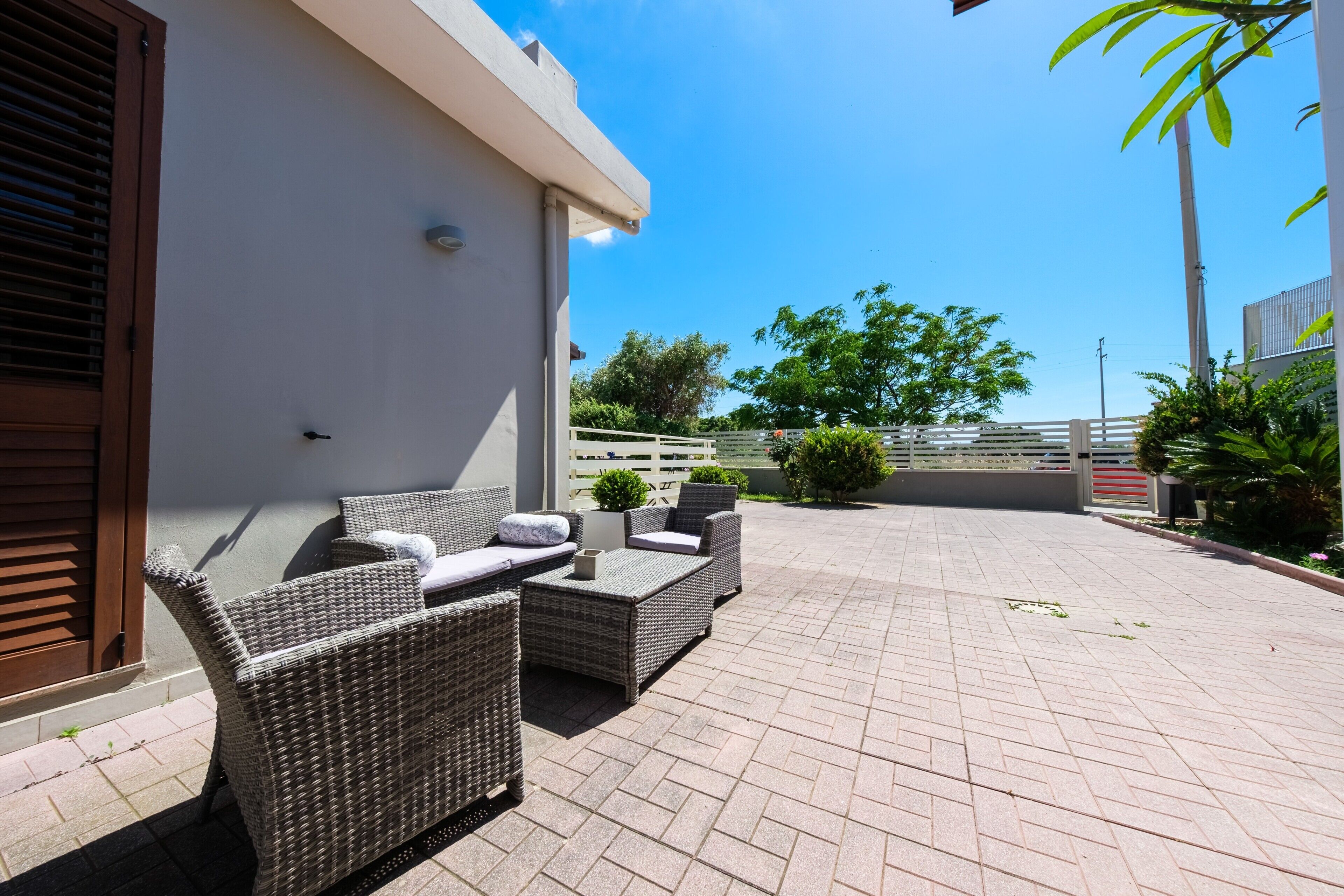 Une terrasse avec des meubles en osier, un mur blanc et un ciel d’un bleu limpide.