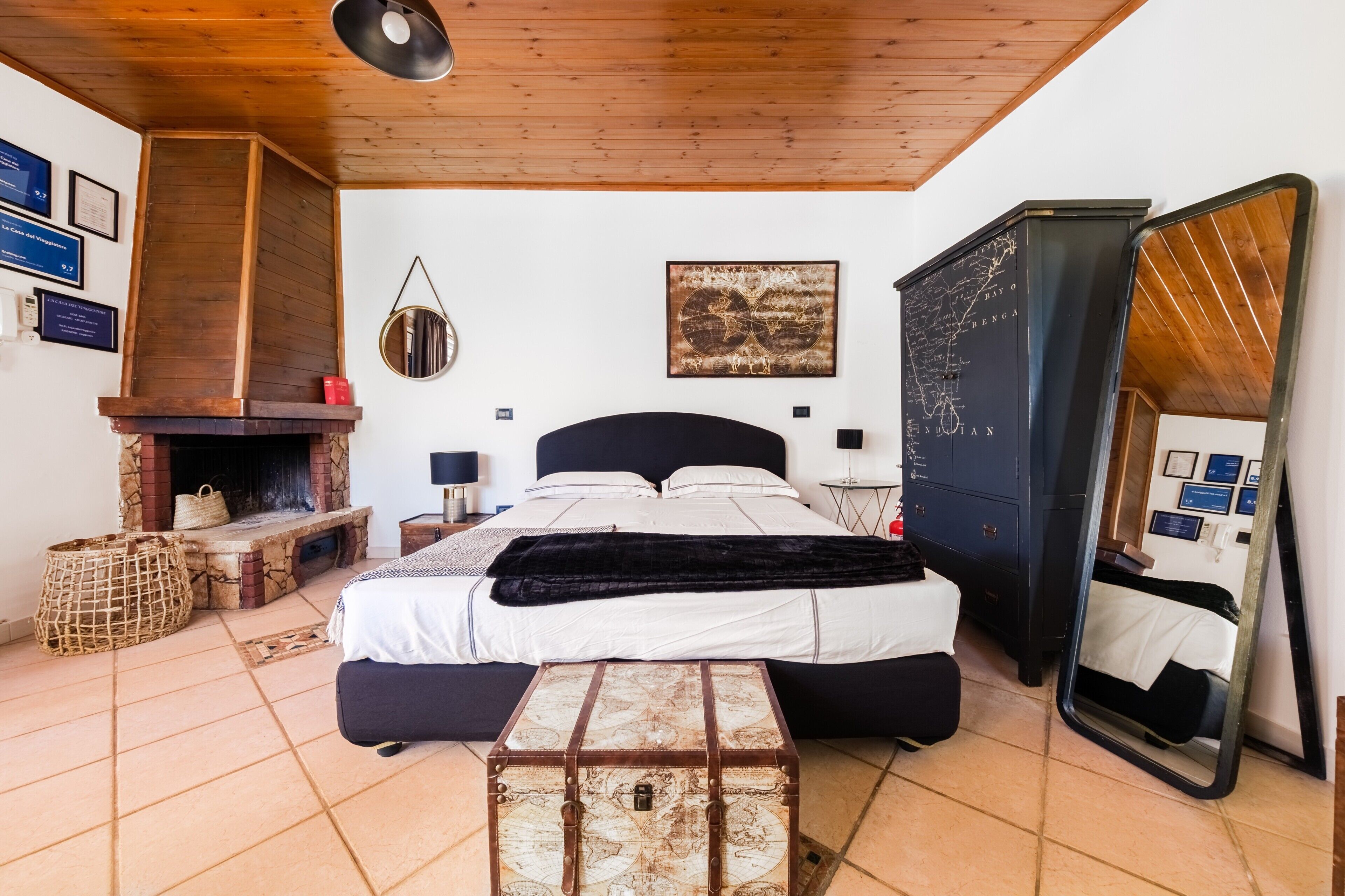 A bedroom with a bed, a fireplace, a mirror, and a map on the wall.