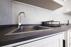 Una cocina con un lavamanos de acero inoxidable, una encimera negra y un armario blanco.