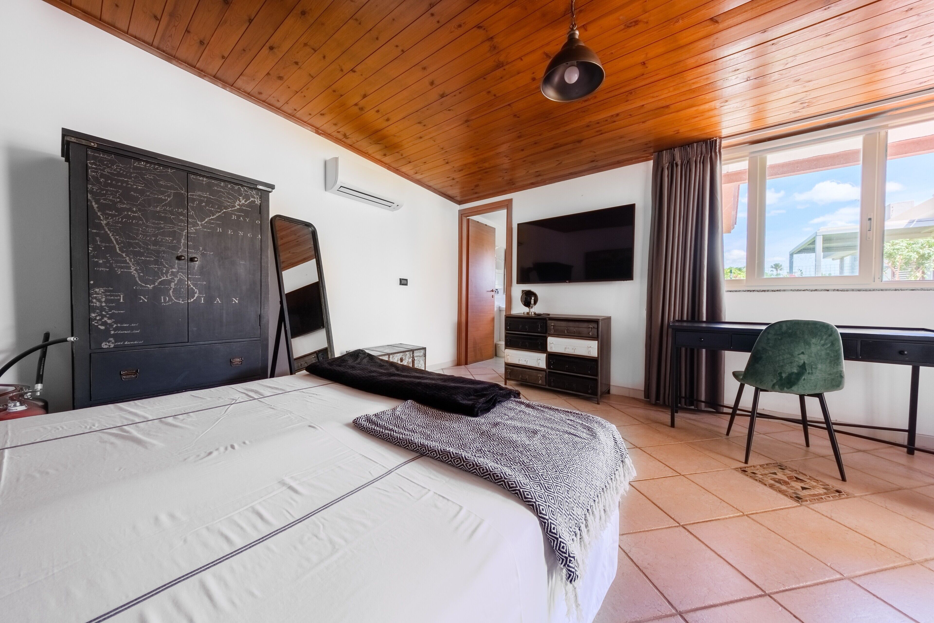 A bedroom with a bed, a map cabinet, a desk, a chair, and a TV.