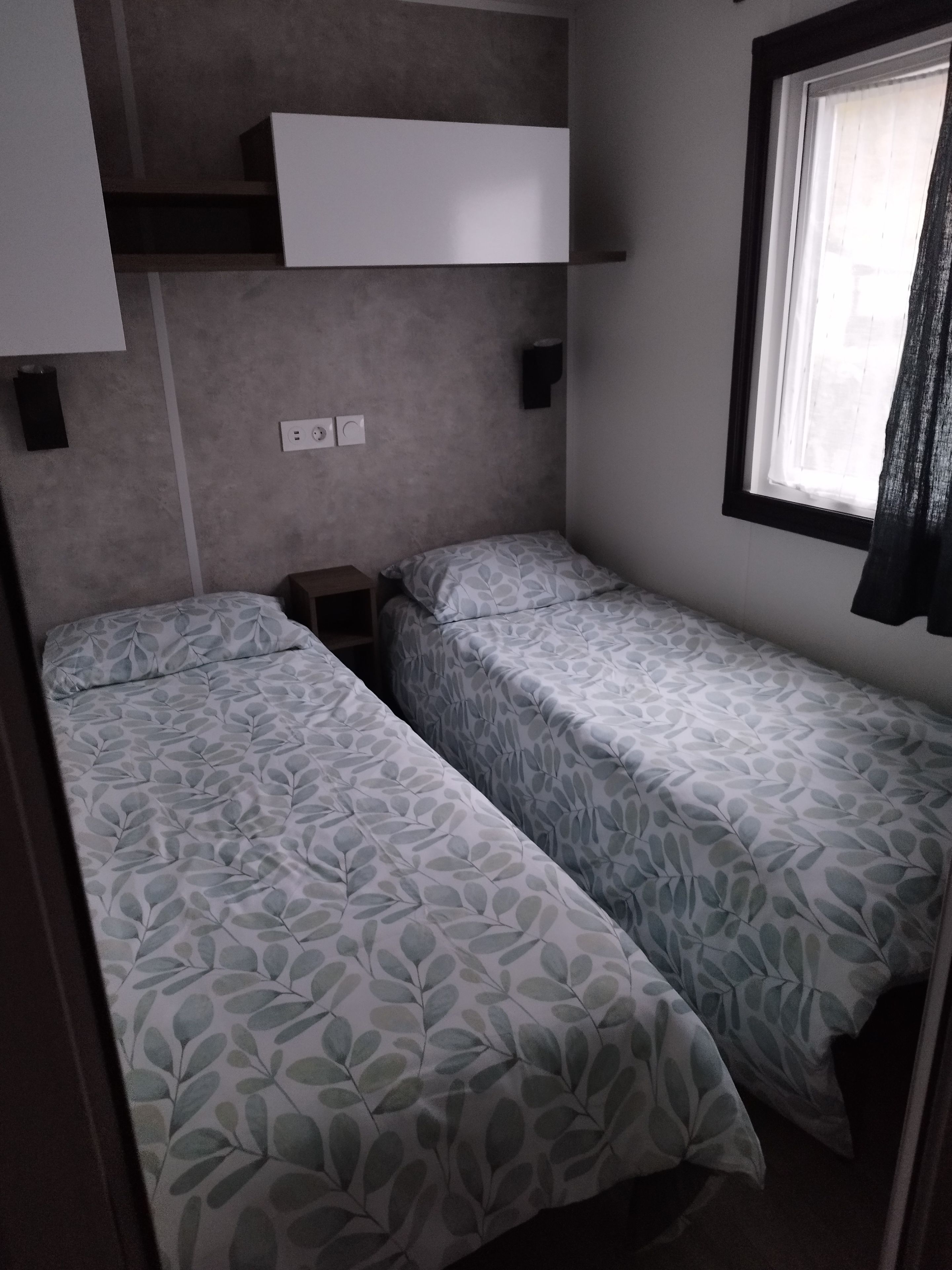 A compact room with two beds, a window, and a white shelf above the beds.