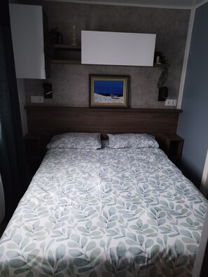 Une chambre à coucher avec un lit, une table de chevet, une étagère avec des objets décoratifs et un tableau encadré au mur.