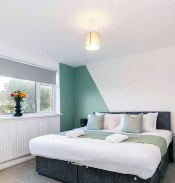 A bedroom with a bed, pillows, a bedside table, a window, and a wall-mounted light fixture. - Modern 3BR Durham Stay for Work Trips (Brandon)