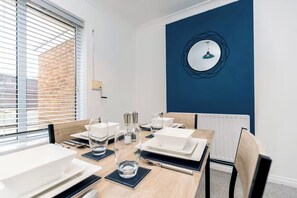 A dining area with a table set for four, a blue accent wall, and a window with blinds. - Modern 3BR Durham Stay for Work Trips (Brandon)