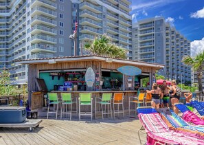 A bar area with a wooden deck, bar stools, and a view of high-rise buildings in the background. - Oceanfront Condo with Sunset Views (Myrtle Beach)