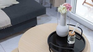 A modern living room with a sofa, a small side table with a lamp, a round table with a tray, and a vase with flowers. - Fresh 1 Bd Apartment with Balcony in Thessaloniki (Thessaloniki)