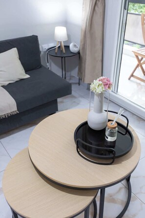 Ett modernt vardagsrum med en soffa, ett litet sidobord med en lampa, ett runt bord med ett bricka och en vas med blommor.