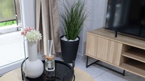 A room with a round table, a potted plant, a vase with flowers, a tray with a candle, and a TV on a wooden stand. - Fresh 1 Bd Apartment with Balcony in Thessaloniki (Thessaloniki)