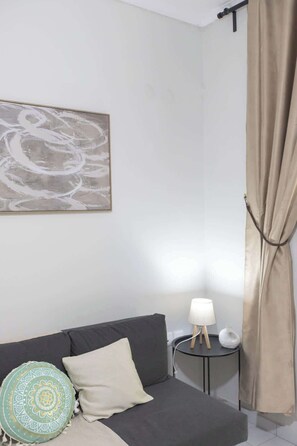 A room with a grey sofa, a round table with a lamp, a beige curtain, and a wall-mounted abstract painting. - Fresh 1 Bd Apartment with Balcony in Thessaloniki (Thessaloniki)