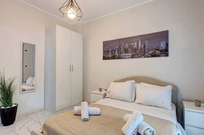 Ett hotellrum med en säng, en målning som föreställer en stadsbild, en garderob, en spegel och en krukväxt.