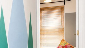Ein Flur mit einer zur Zimmerführenden Tür, einem Sessel mit einem Blumenkissen und einem Fenster mit Jalousien.