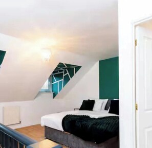 Ein modernes Schlafzimmer mit schrägem Dach, einem Bett mit schwarz-weißer Bettwäsche und einem Fenster mit geometrischem Muster.