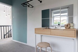 Ein Zimmer mit Schreibtisch, Stuhl, Fenster und einer Pendelleuchte.