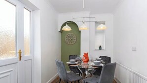Comedor con mesa de vidrio, cuatro sillas, un reloj y lámparas colgantes.
