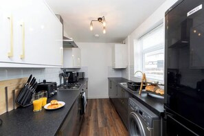 Eine moderne Küche mit Herd, Mikrowelle und Backofen, einem Spülbecken und einem Fenster mit Jalousien.
