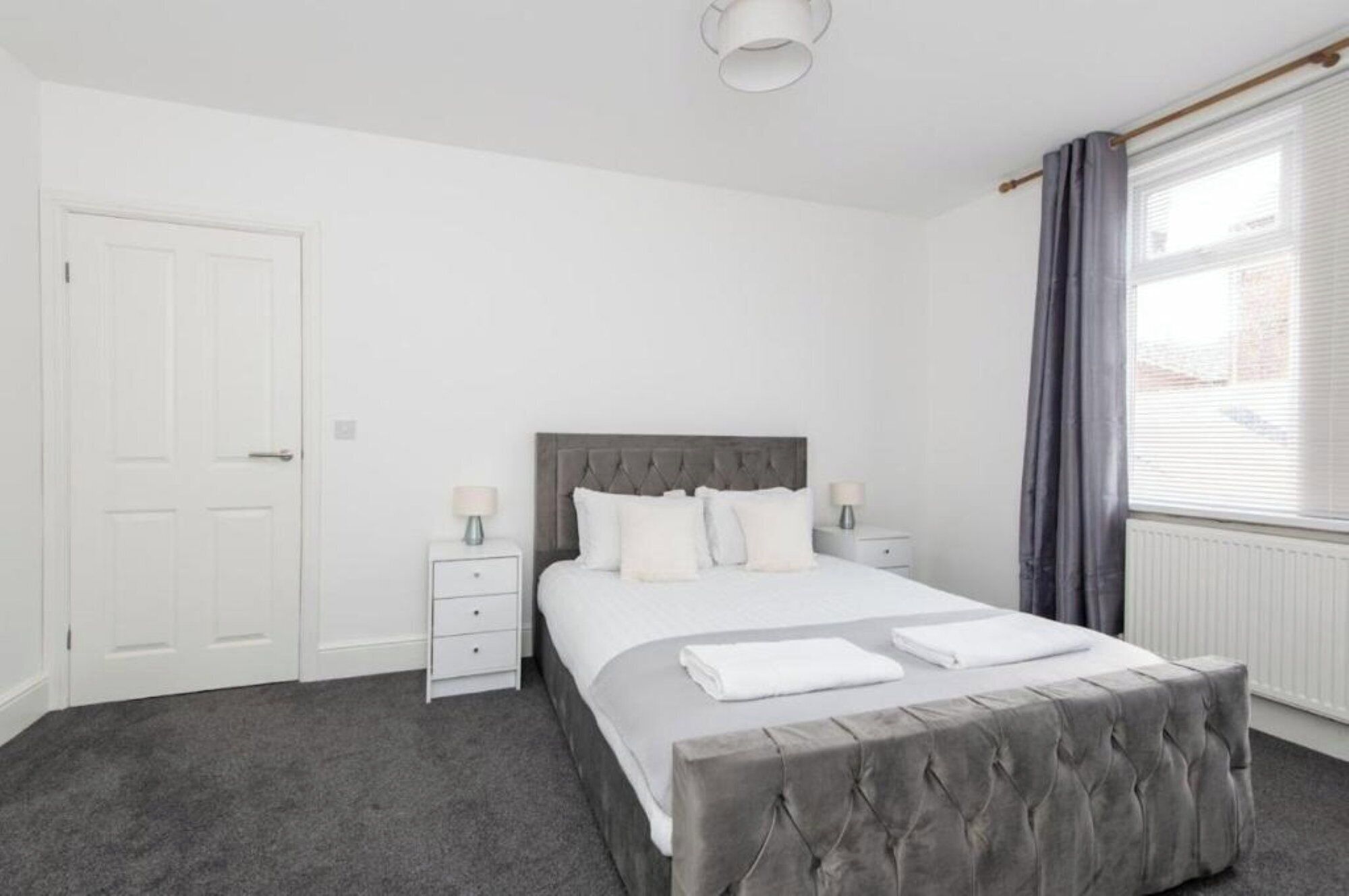 A bedroom with a bed, two bedside tables, a window with curtains, and a door.