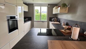 Une cuisine moderne dotée d’un grand îlot central, d’appareils électroménagers intégrés et offrant une vue sur la verdure environnante.