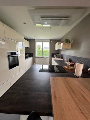 A modern kitchen with a large island, built-in appliances, and a view of greenery outside. - Entre Terre et Mer Maion family 12/14 persons with heated pool and dome (Landivisiau)