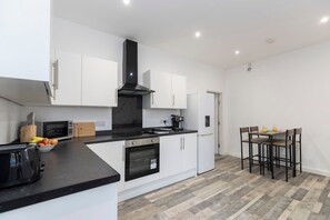 Une cuisine moderne avec des meubles blancs, une hotte noire, un four à micro-ondes, un four traditionnel et un coin repas avec une table et des chaises.