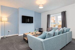 Een moderne woonkamer met een bank, een flatscreen televisie, een lamp en een eettafel.