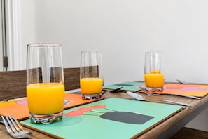 Een tafel met drie glazen sinaasappelsap, een vork en een lepel, gezet op een tafel met kleurrijke placemats.