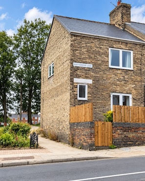 A two-story brick house with a visible front door, a wooden fence, and a sign reading 'Northumberland Land.' - Your Perfect 3-Bed Stay Near Durham University (Ushaw Moor)