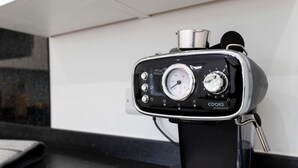 A coffee maker with a pressure gauge and control knobs, a metal container on top, and a black base.