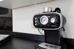 A coffee maker with a pressure gauge and control knobs, a metal container on top, and a black base.