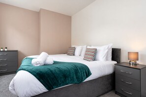 Een moderne hotelkamer met een bed, nachtkastje, lamp en dressoir.