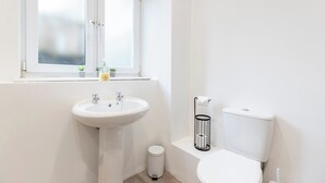 A small, modern bathroom with a white sink, toilet, and window.