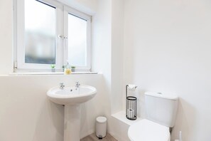A small, modern bathroom with a white sink, toilet, and window.