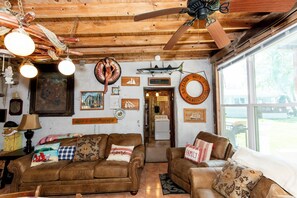 A rustic interior with wooden beams, a ceiling fan, and a large window. - Historic Lakefront Homestead on Kelleys Island (Kelleys Island)