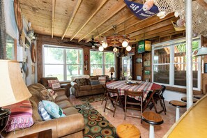 A cozy living room with a wooden ceiling, a dining table with chairs, and a large window. - Historic Lakefront Homestead on Kelleys Island (Kelleys Island)
