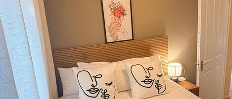 A bedroom with a bed, two pillows with a face design, a framed picture on the wall, a bedside lamp, and a door.
