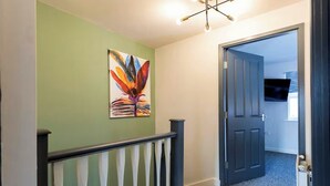 Een gang met een groene muur, een schilderij van een bloem, een trap met witte spijlen, en een deur die naar een andere kamer leidt.