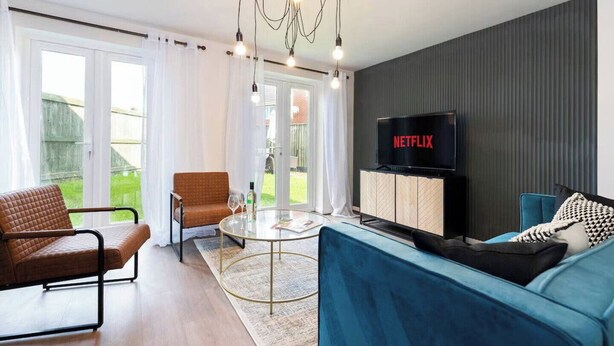 Een moderne woonkamer met een bank, fauteuil en een televisie waarop 'NETFLIX' wordt weergegeven.