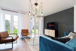 Ein modernes Wohnzimmer mit einer Couch, einem Sessel und einem Fernseher, der 'NETFLIX' anzeigt.