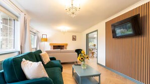 A living room with a green sofa, a coffee table, a TV mounted on a wooden wall, and a fireplace. - Hot Tub/ Free Parking/ 5 Bedroom/ Large Space (Low Coniscliffe)
