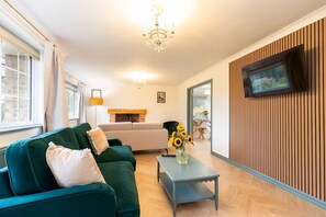 Ein Wohnzimmer mit einem grünen Sofa, einem Couchtisch, einem an einer Holzwand montierten Fernseher und einem Kamin.