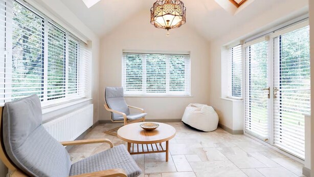 A spacious room with a high ceiling, large windows, a round wooden table, a comfortable chair, and a unique chandelier. - Hot Tub/ Free Parking/ 5 Bedroom/ Large Space (Low Coniscliffe)