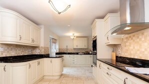 A kitchen with white cabinetry, black countertops, a glass backsplash, and a stainless steel range hood. - Hot Tub/ Free Parking/ 5 Bedroom/ Large Space (Low Coniscliffe)