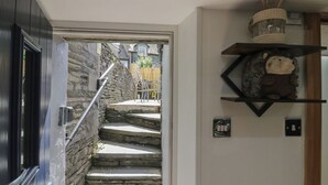 Eine Treppe führt zu einer Steinsäule, einer schwarzen Tür und einem Regal mit einem Dekorationsgegenstand.