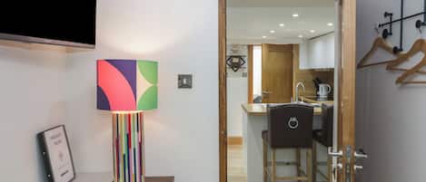 A room with a desk, a colorful lamp, a fire safety folder, and a view into a kitchen area.