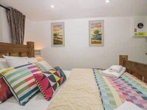 Ein Schlafzimmer mit einem hölzernen Kopfende, einem Bett mit farbenfrohen Kissen, einer Steude und zwei gerahmten Landschaftsbildern an der Wand.