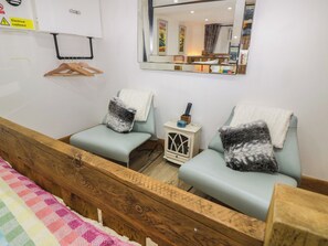 A room with two light blue chairs, each with a white towel and a gray pillow. A small white cabinet with a glass door and a remote control on top is next to the chairs. - Park View Studio (Ambleside)