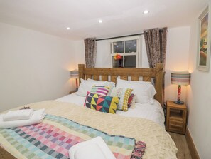 A bedroom with a wooden bed, white bedding, a window with curtains, a bedside lamp, and a wall-mounted picture. - Park View Studio (Ambleside)