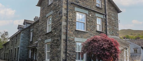 A stone building with multiple windows and a small tree with red foliage.