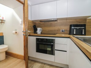 A compact kitchen with white cabinets, a wooden countertop, a coffee maker, a toaster, and a dishwasher. - Park View Studio (Ambleside)